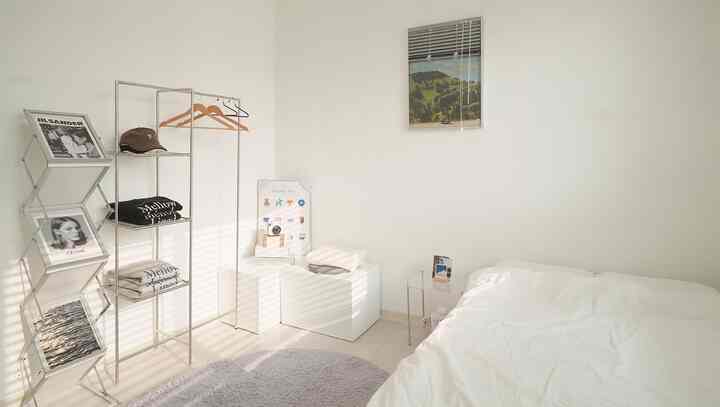 A simple white and silver toned bedroom featuring shelves and picture frames in a modern minimal interior