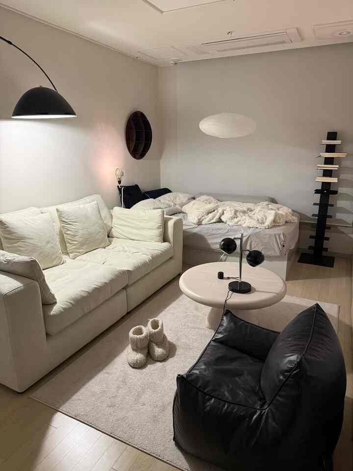 アイボリーとブラックのトーンが特徴的な一人暮らし向けのナチュラルモダンな寝室兼リビング、ソファとビーンバッグ、丸いコーヒーテーブルが配置された落ち着いた空間
