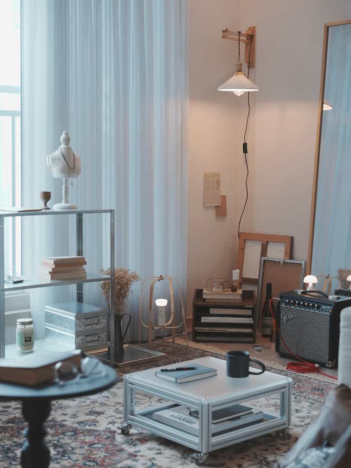 白い壁と木目調の照明が調和するリビング、シルバーの金属棚とテーブルが配置された雰囲気のあるヴィンテージ空間