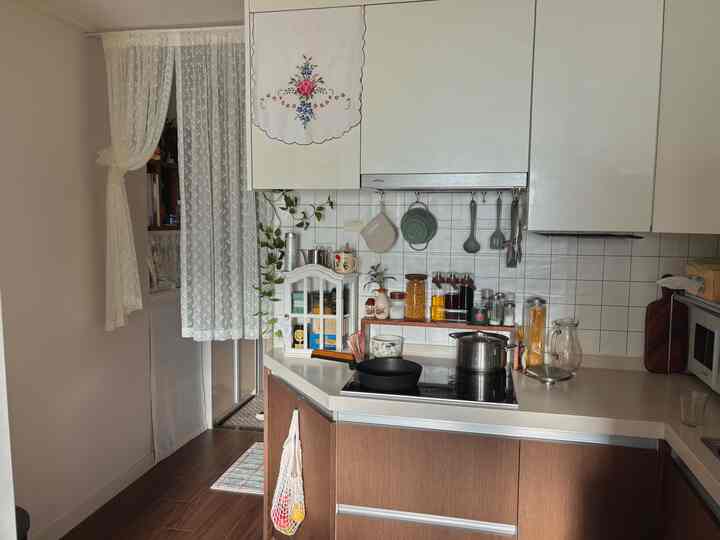 ホワイトと木目調が調和するナチュラルモダンなキッチン、レースカーテンとレトロな小物が温かみのある雰囲気を演出する空間