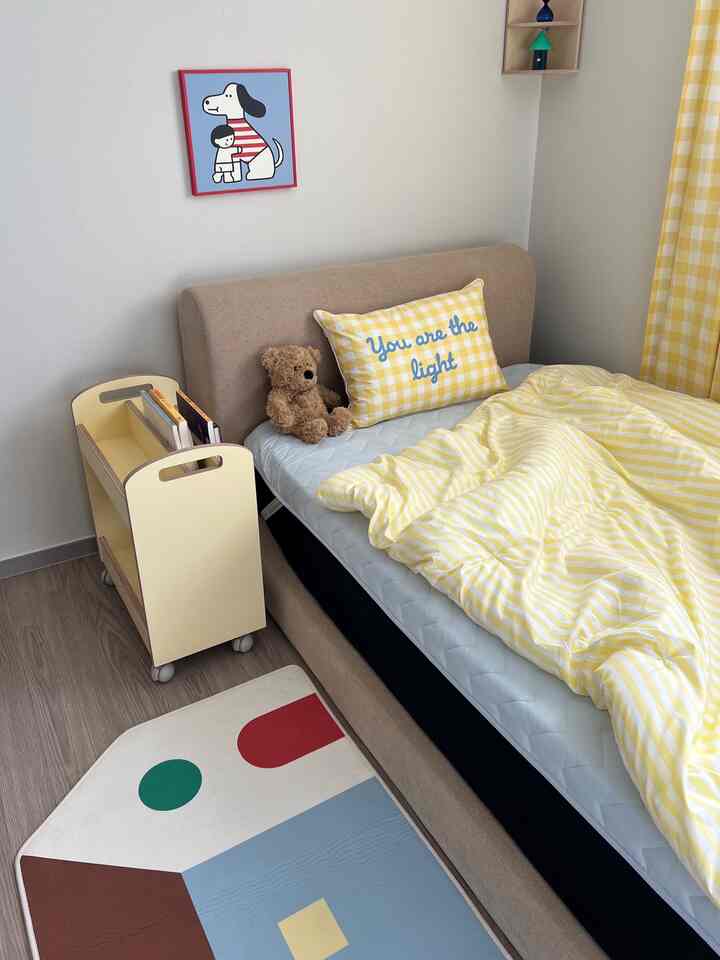 黄色のチェック柄寝具とベージュのベッドがある子供部屋、テディベアとカラフルなラグが温かみのある雰囲気を演出している