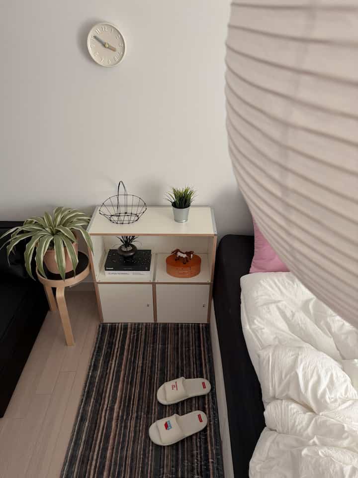 ナチュラルカラーのコンパクトで狭い寝室、ベッドとナイトテーブル、ソファが配置された雰囲気のある空間