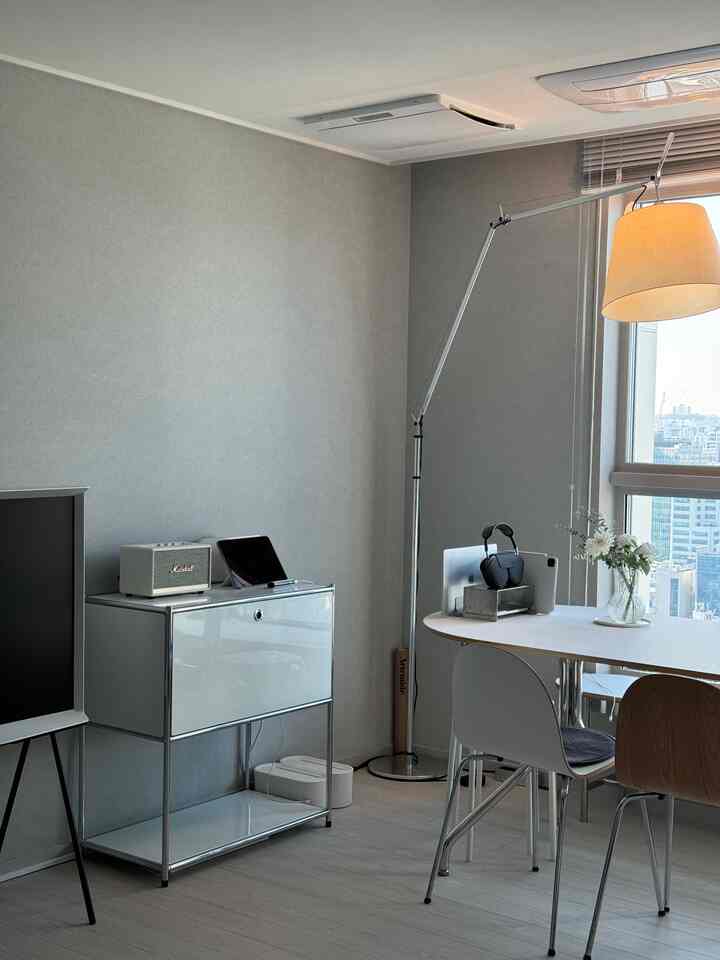 白と木目調のリビング、窓際に配置された大きな白のオーバルダイニングテーブルとマーケットBの収納棚、フロアランプが調和した清潔感のある明るい空間