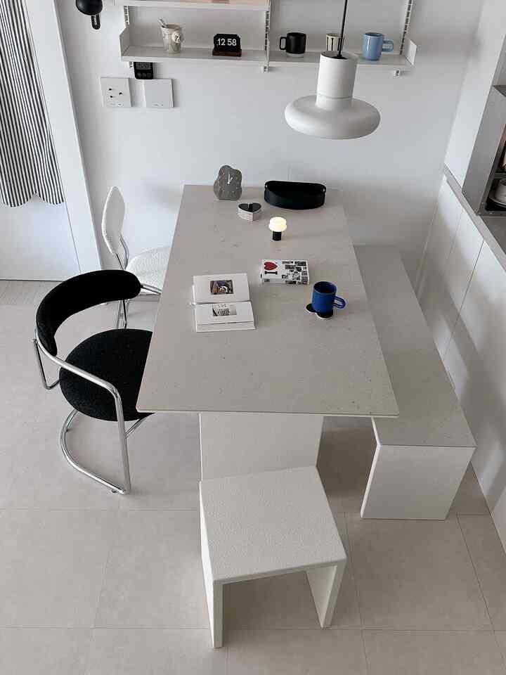 ホワイトとブラックの色調のダイニングルーム、ブークレ椅子と大きなセラミックダイニングテーブルが配置されたシンプルでミニマルなカフェ風インテリア