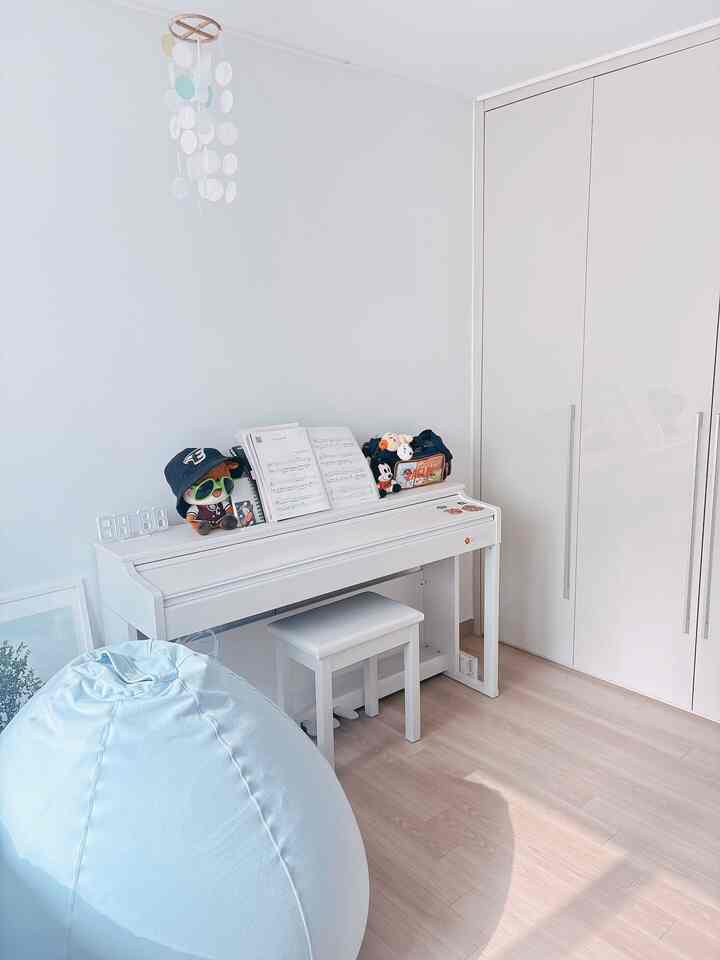 明るい白と木目調フロアの子供部屋、デジタルピアノと淡い青のビーズクッションが配置されたモダンな空間