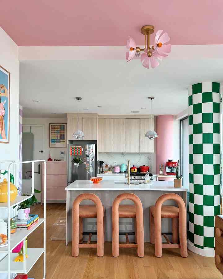 Bright, modern kitchen featuring a pink ceiling and green checkered pillar, soft curved peach bar stools, and a white kitchen island