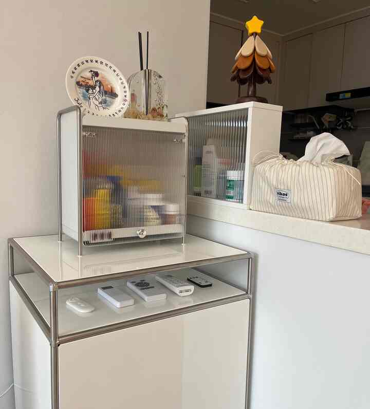 白を基調としたリビング横のキッチンスペースに、ナイトテーブルと栄養剤収納キャビネット、ティッシュケースが配置されたモダンなインテリア