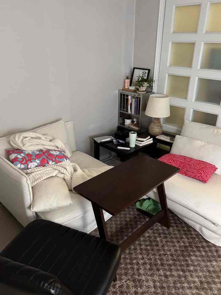 アイボリー色調のワンルームリビング、2つの白いソファと黒い革製椅子、ブラウンのラグ、照明が配置された居心地の良い空間