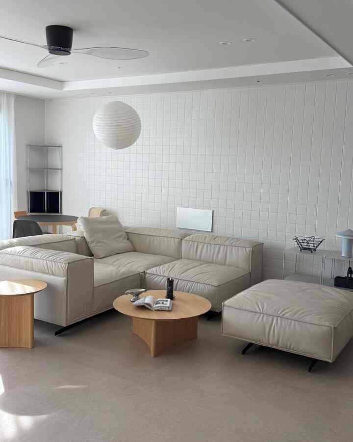 白いタイル壁とベージュのレザーコーナーソファ、木製テーブルが配置されたナチュラルモダンなリビングルーム