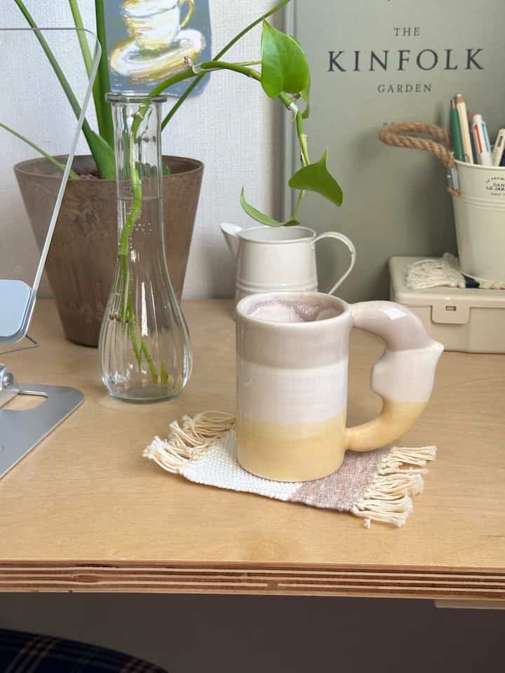 ナチュラルな色調のテーブルの上に植物とマグが置かれたホームオフィスのコーナー