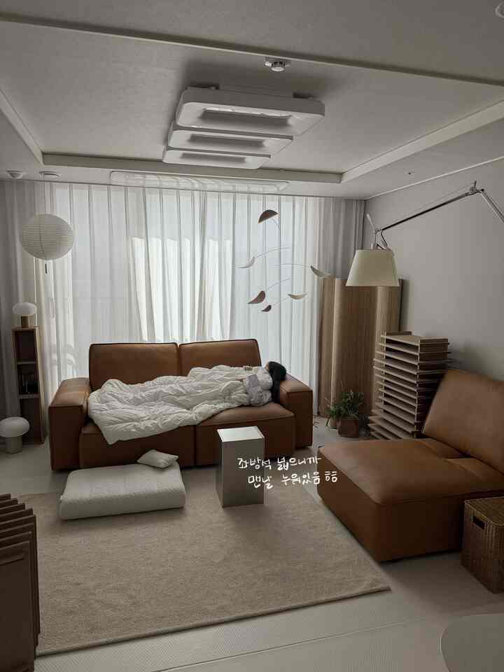 ブラウンのレザーで作られたモジュラーソファとナチュラルモダンなリビング、広い座席とペーパーランプ、インテリアモビールが配置された温かみのある空間