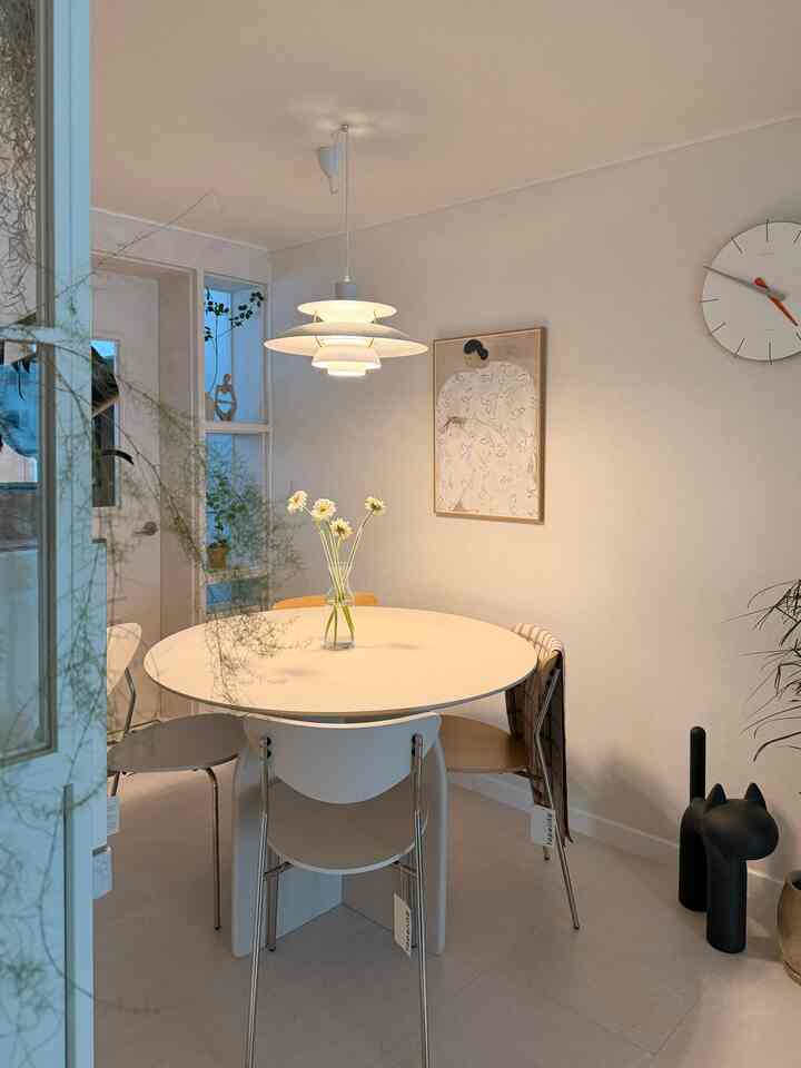 柔らかな白とベージュの色調のキッチンダイニング、円形テーブルとペンダントライト、花と猫のオブジェが配置された雰囲気のある空間