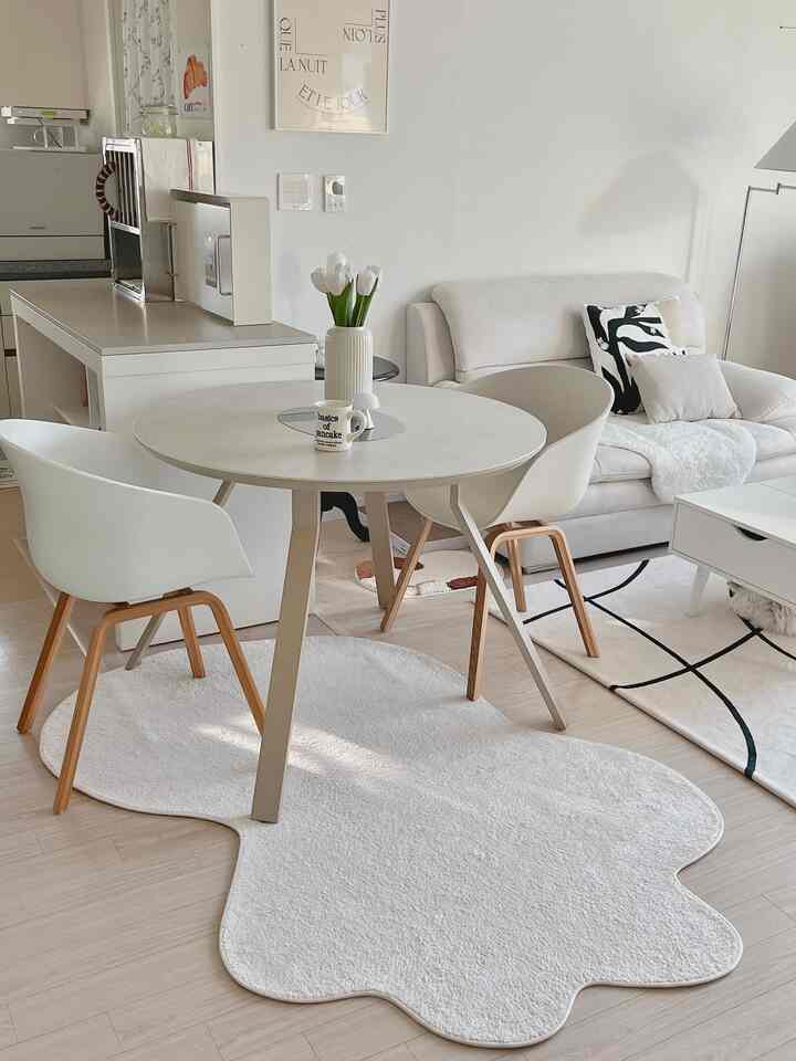 White and natural toned kitchen-dining space featuring a round dining table and irregular rug, creating a cozy atmosphere