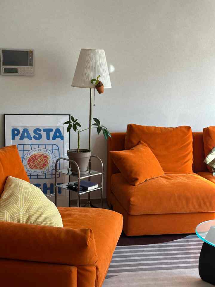 オレンジのソファとステンレス製のサイドテーブルが配置されたモダンな雰囲気のリビング