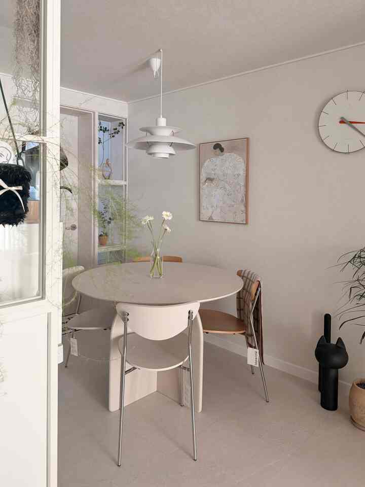 ホワイトとウッドトーンが調和したダイニングスペース、円形のテーブルと椅子、ペンダントライト、植物が配された印象的な空間