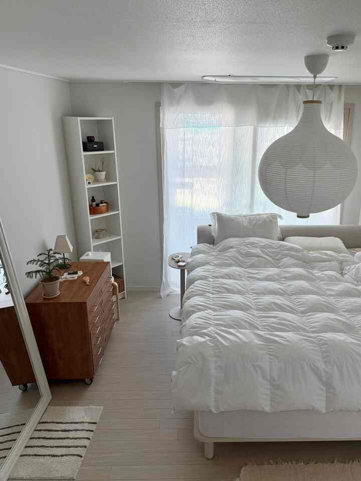 ホワイトとウッドトーンが調和したシンプルな寝室、快適なベッドとチェストが配置された落ち着いたインテリア