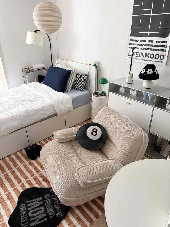 ホワイトとベージュのトーンのワンルーム寝室、ベッドとベージュのソファ、ネイビーのパターンクッションが配置された雰囲気のあるインテリア