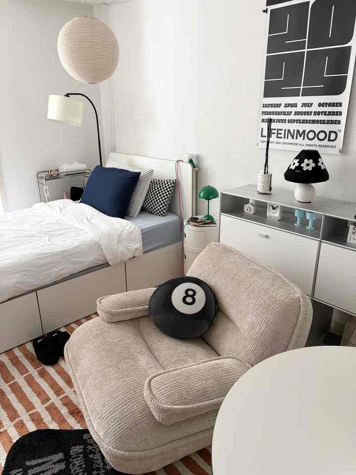 白とナチュラルトーンの寝室、ベージュのソファとネイビーのクッションが調和した印象的な空間