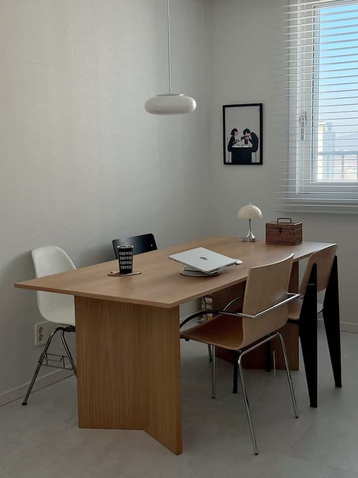 Modern dining room with white and wood tones, featuring a wooden dining table, chairs, window blinds, and pendant light in a clean setting
