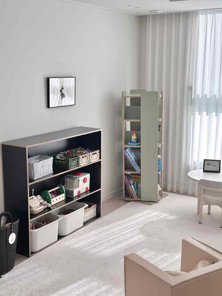 ベージュとホワイトの色調の子供部屋、おもちゃ収納棚と小さな子供用テーブルが配置されたすっきりとしたコンパクトな空間