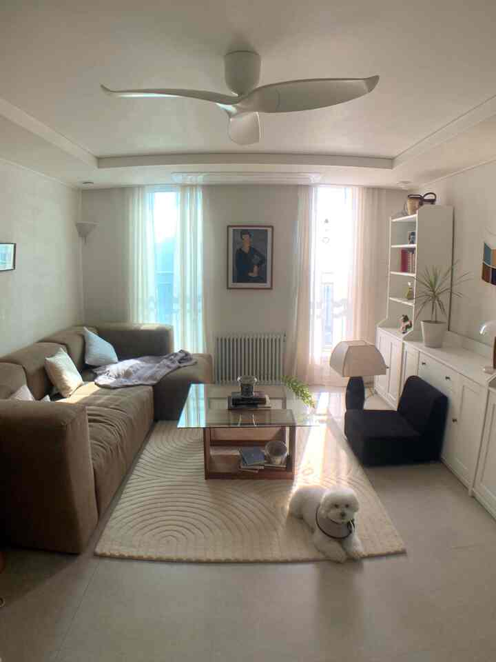 アイボリーとブラウンの色調のリビング、ブラウンのソファとガラスのコーヒーテーブル、窓から自然光が差し込む落ち着いた雰囲気のインテリア