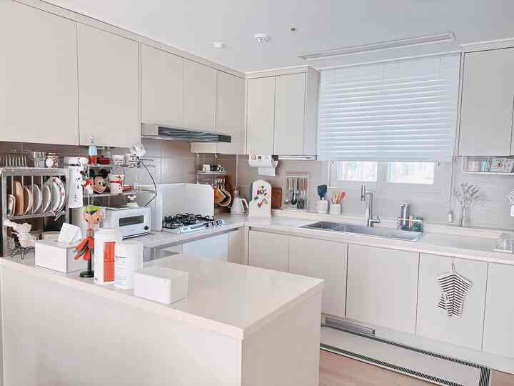 明るい白を基調とした木製の床を持つキッチン空間、整然とした収納とシンプルモダンなインテリア