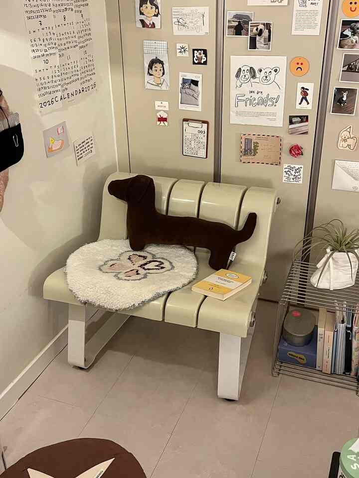 ベージュの小さな書斎空間、犬の形のクッションとベージュのベンチ、本と植物が配置された雰囲気のあるインテリア