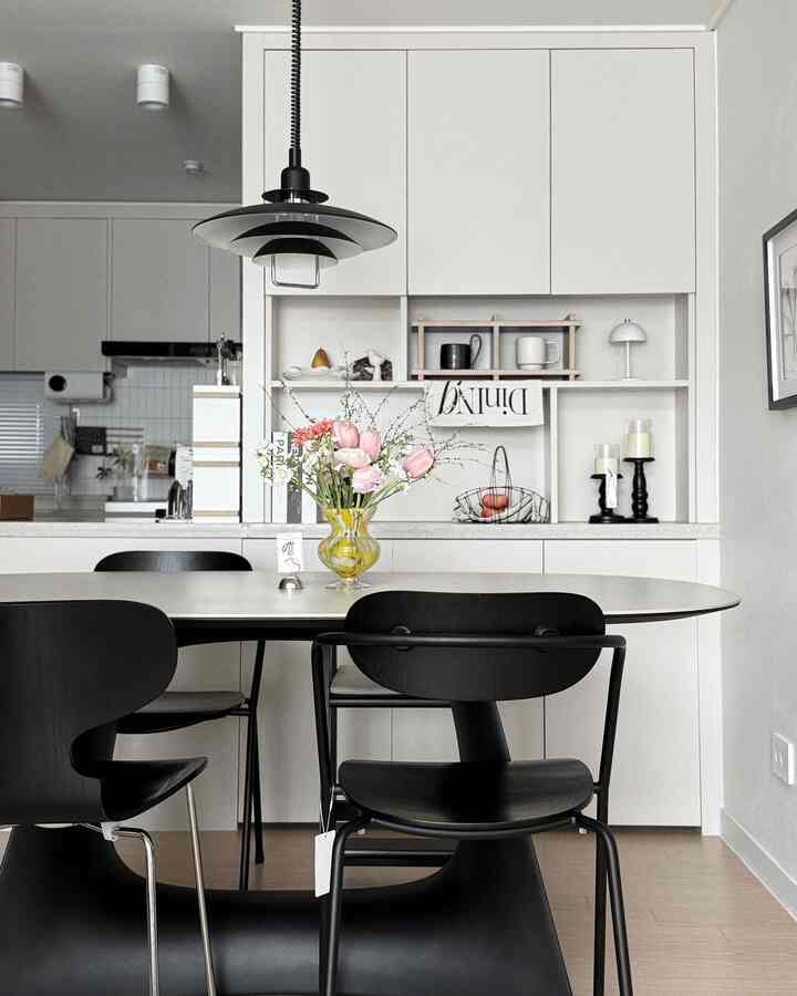 白い壁とナチュラルな木製フローリングのダイニングスペース、黒いダイニングチェアとペンダントライトが配され、モダンで自然な雰囲気のインテリア