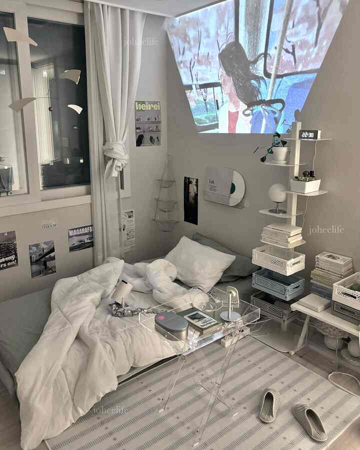 白とナチュラルな色調の寝室、ベッドと遮光カーテン、ビームプロジェクターが配置された印象的な空間