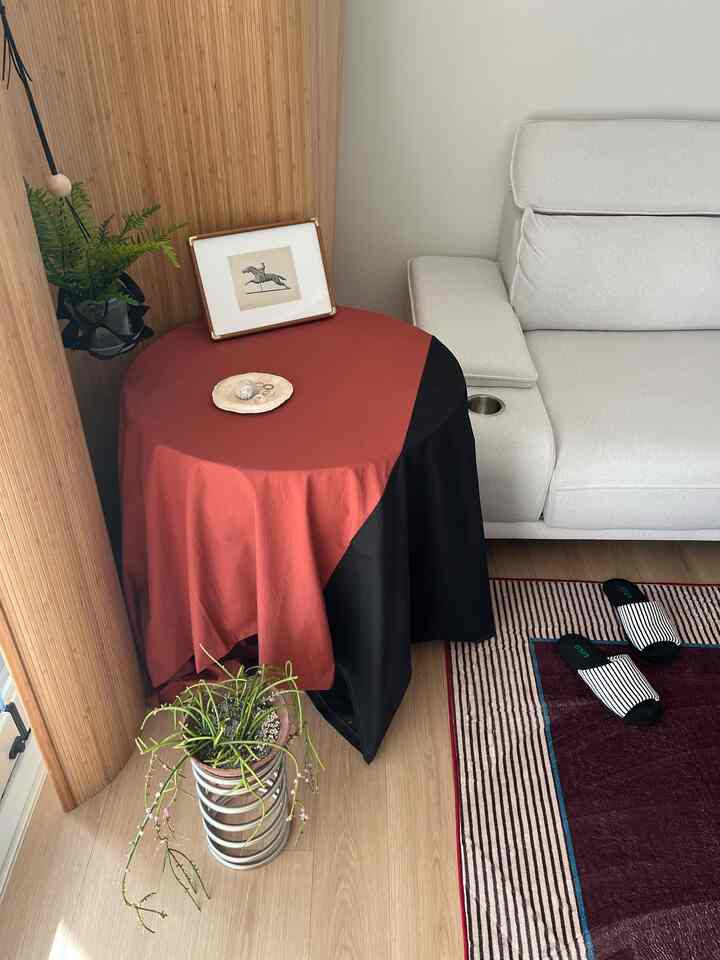 ブラウンの木目調壁と白いソファ、赤と黒のクロスを掛けた丸テーブルが配置されたモダンで自然なリビング