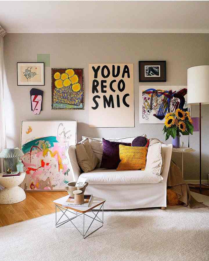Natural colored walls and a white sofa with colorful posters and cushions in an art-inspired living room