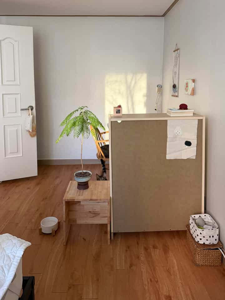 ナチュラルな色調のリビング、木目調のサイドテーブルと植物が置かれ、テーブルの後ろに猫が隠れている雰囲気のあるインテリア