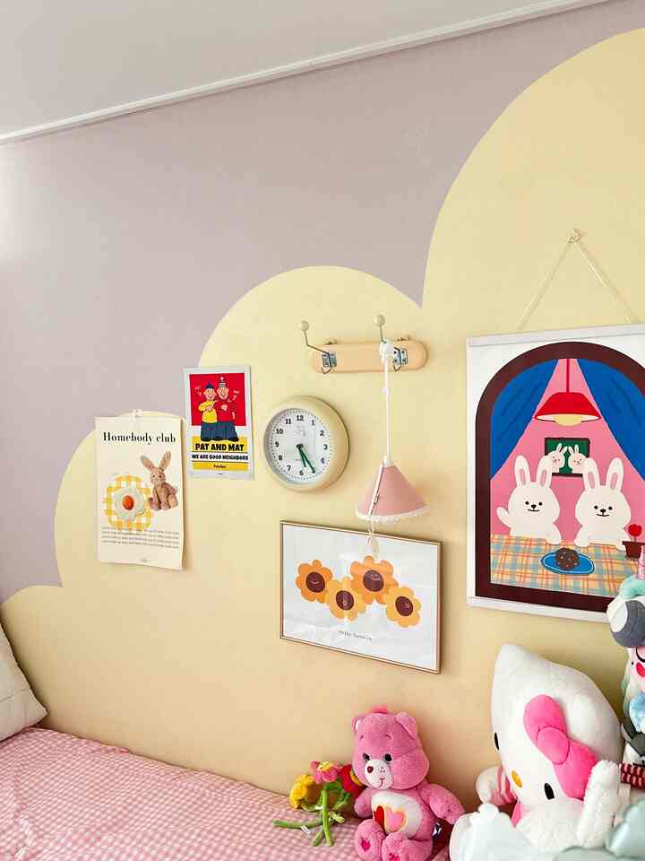 ベージュとピンクの色調の子供部屋、壁にはかわいいポスターと時計が掛かり、ピンクの寝具とぬいぐるみが配置された暖かい雰囲気の空間