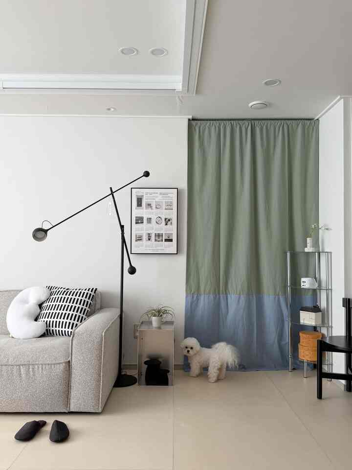 グリーンとブルーのツートーンカーテンがあるモダンなリビングルーム、シンプルなソファと黒いフロアランプが配置された落ち着いた空間