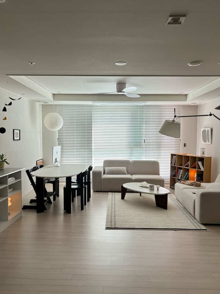 明るくナチュラルな色調のリビング、ベージュのソファと木製の本棚が配置されたシンプルで居心地の良いインテリア