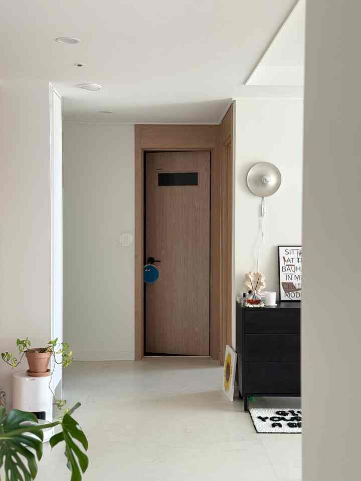 白とナチュラルウッドの調和が取れた玄関、シンプルでモダンな額縁と壁付け照明が配置された清潔感のあるインテリア