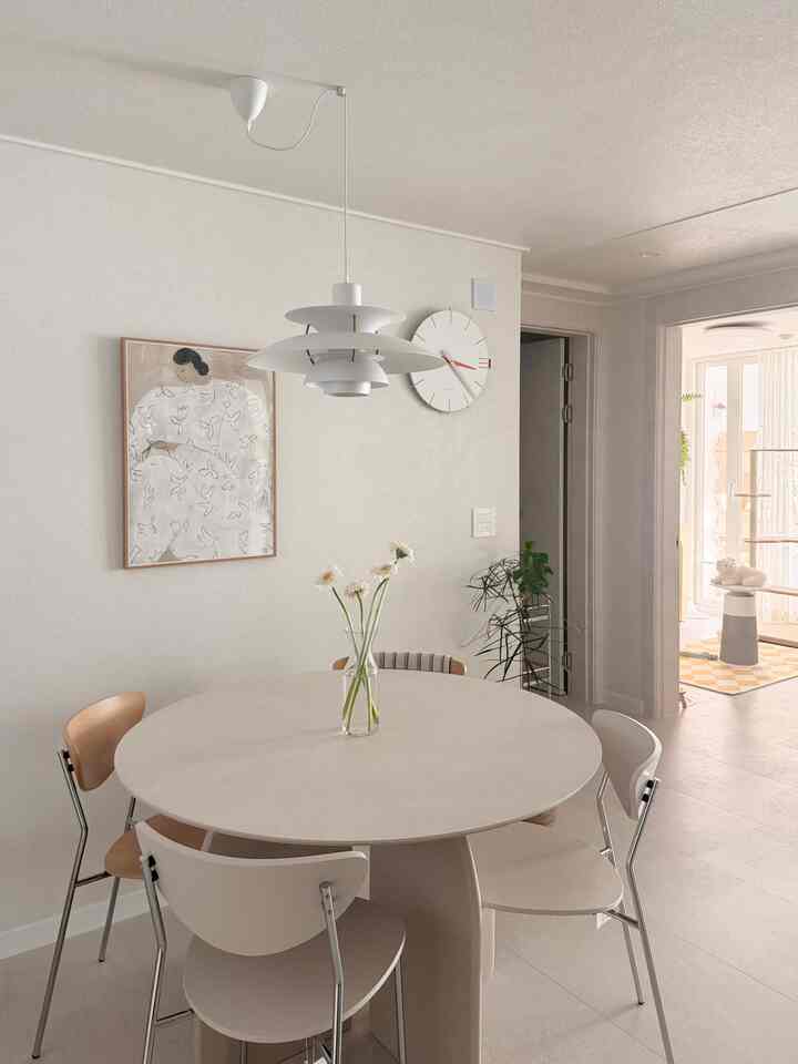 白とベージュのトーンのダイニングルーム、中央に丸いダイニングテーブルと花が置かれた印象的なインテリア