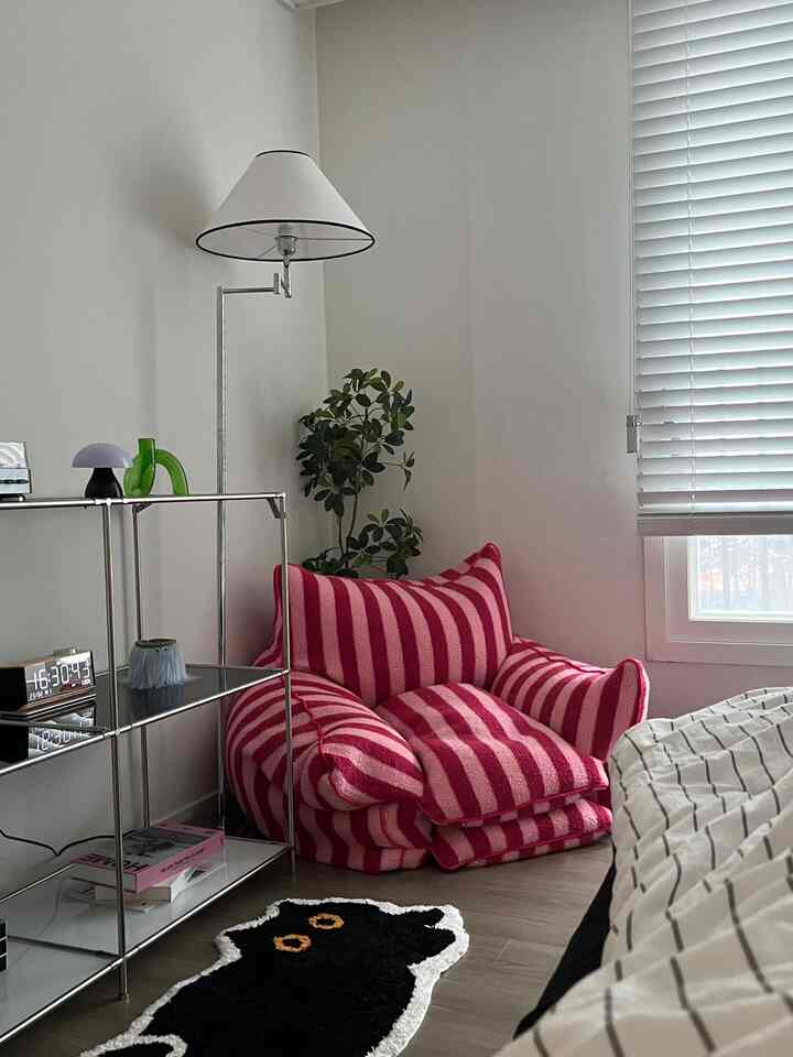 白い壁とブラインド、ピンクのストライプのビーンバッグと黒猫の形のラグが配された雰囲気のある寝室の一角