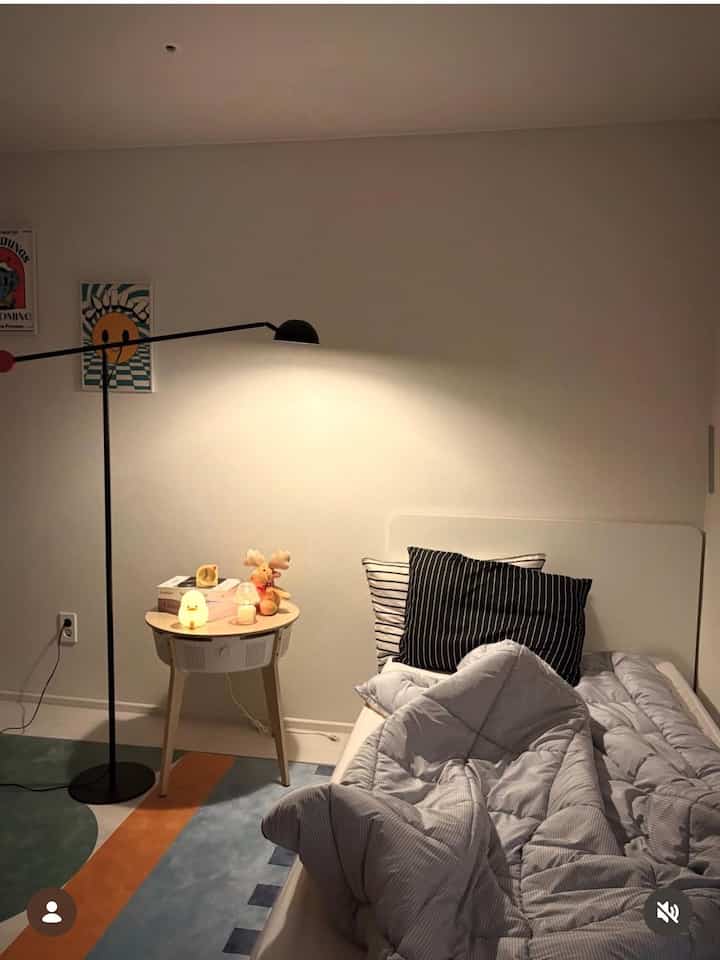 白とナチュラルの色調の子供部屋、整ったベッドとラグ、ナイトテーブルとフロアランプが雰囲気のあるインテリア