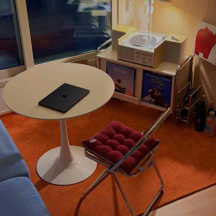 オレンジ色のラグとブルーのソファが調和した二部屋のリビング、丸いダイニングテーブルとレトロなターンテーブルが配置された印象的な空間