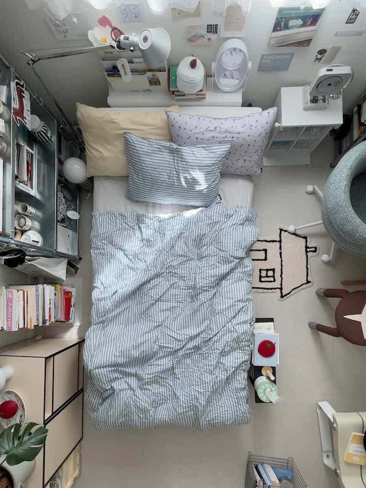 ホワイトとブルーのトーンでまとめられた小さな寝室、ベッド、枕、本棚、照明が配置された雰囲気のあるインテリア