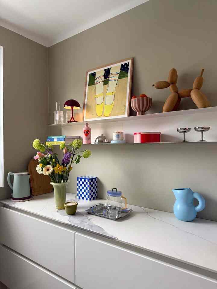 Beige and white toned kitchen shelf space featuring a vase of fresh flowers and playful decorative objets with a cozy styling vibe