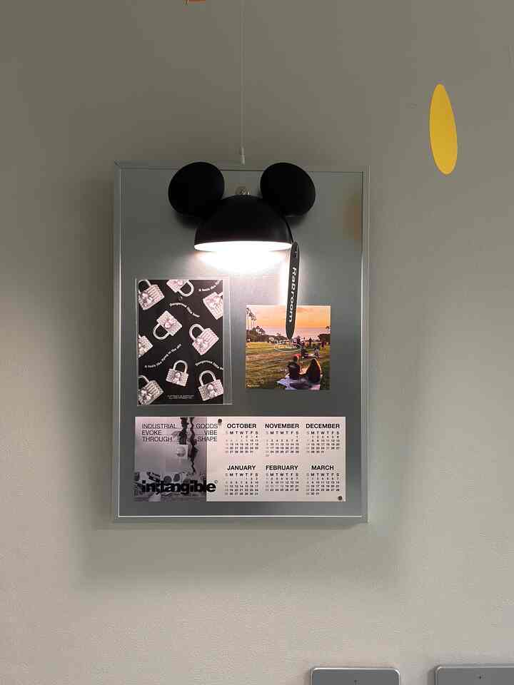 シルバーの額縁磁気ボードが中央の壁に掛かり、上に黒いミッキーマウスのブラケットライトがあるシンプルでモダンなインテリア空間