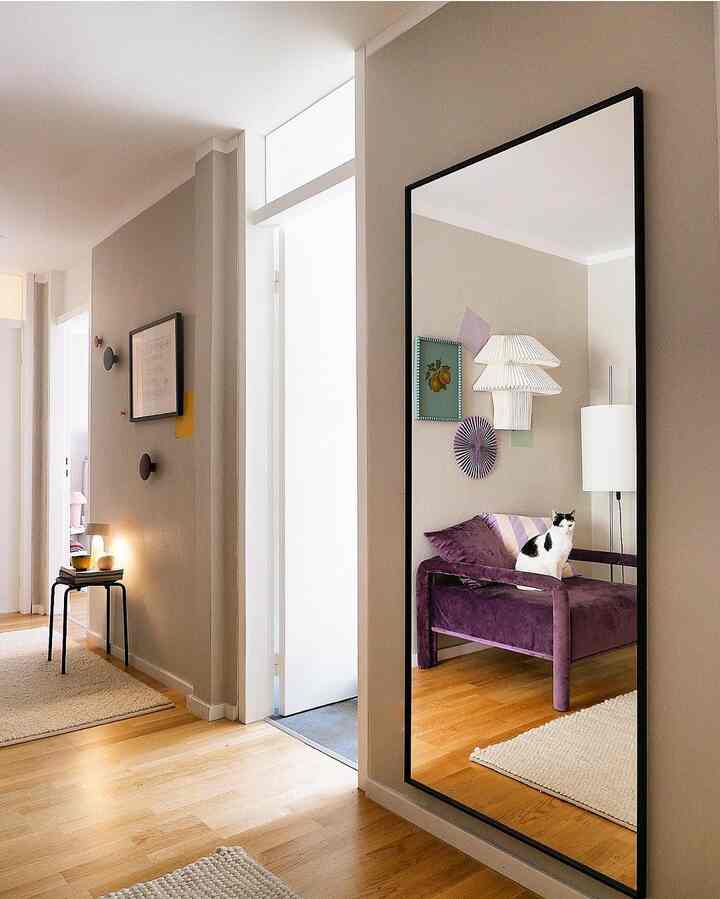 Natural-toned hallway with wood flooring, featuring a large full-length mirror and a purple velvet sofa with a cat, creating a cozy atmosphere