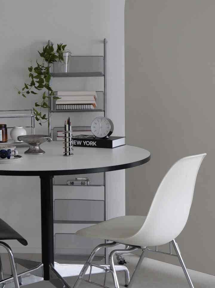 White and gray toned dining room featuring a minimalist round table and metal shelving unit with a clean atmosphere