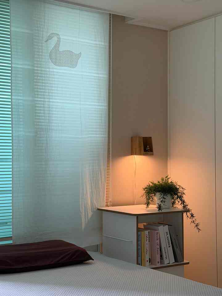 ホワイトと木目調が調和した寝室、スリムなナイトテーブル兼書棚が置かれた落ち着いた印象のインテリア