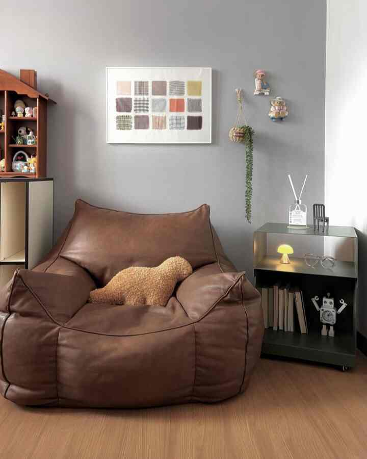 ナチュラルな色調のリビング、ブラウンのビーズクッションソファとグレーの壁、棚が配置された雰囲気のあるインテリア