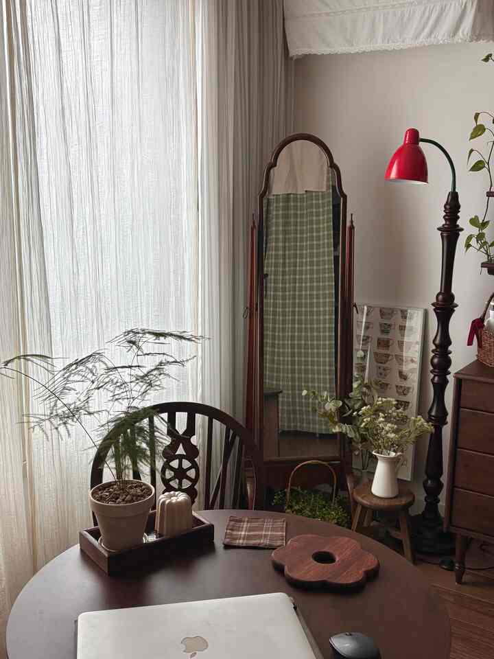 自然光が差し込むナチュラルな木目調リビング、丸い木製テーブルと全身鏡、フロアランプが温かみのあるヴィンテージな印象の空間