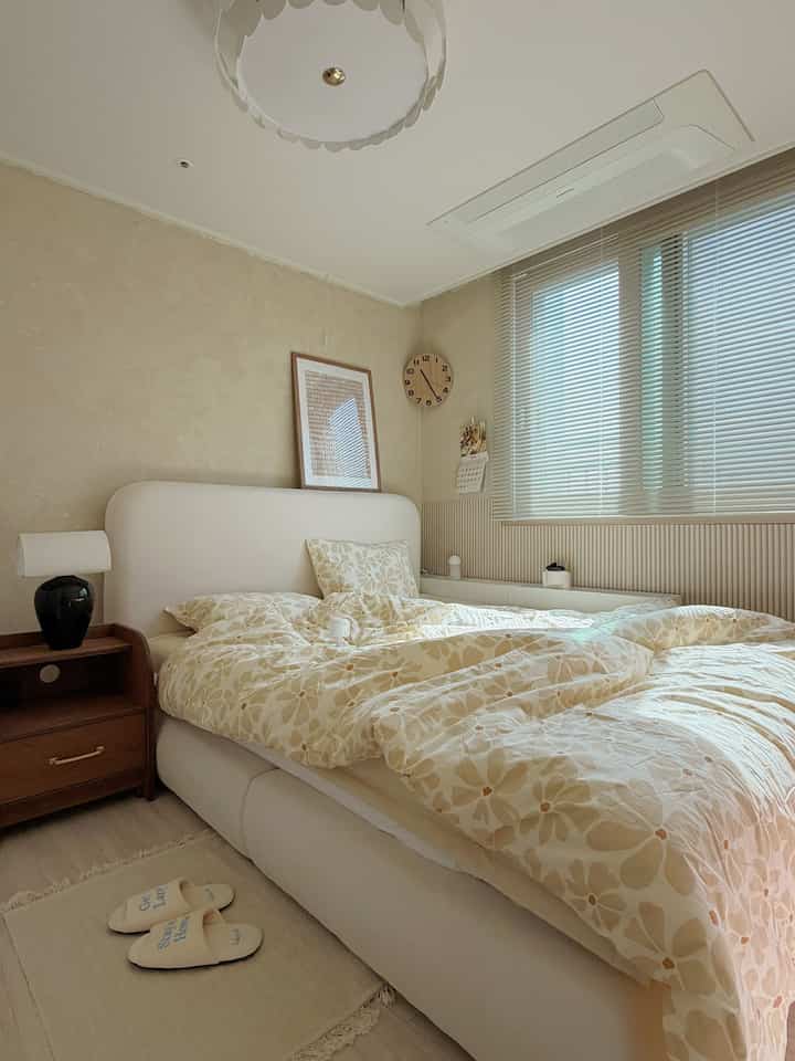 ベージュのトーンの寝室、ホワイトのベッドフレームとベージュの柄布団が配置された温かく居心地の良いインテリア