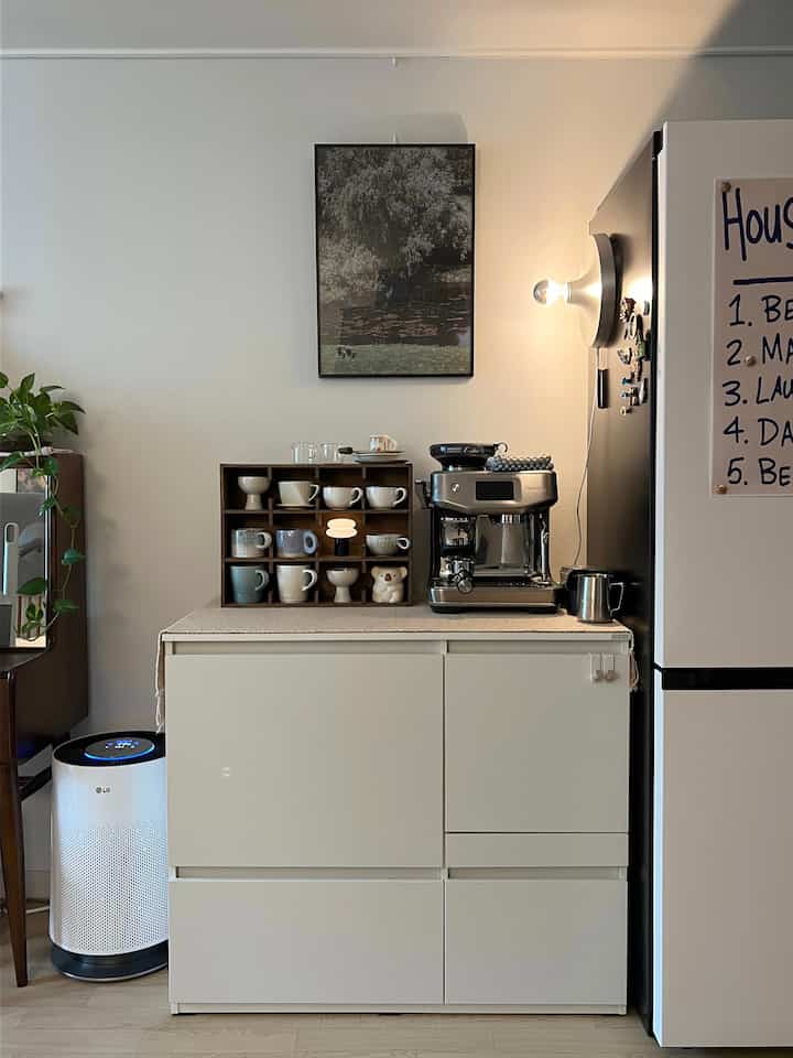 白と茶色のトーンのワンルームキッチン、コーヒーマシンとカップ棚が配置された雰囲気あるおうちカフェ空間